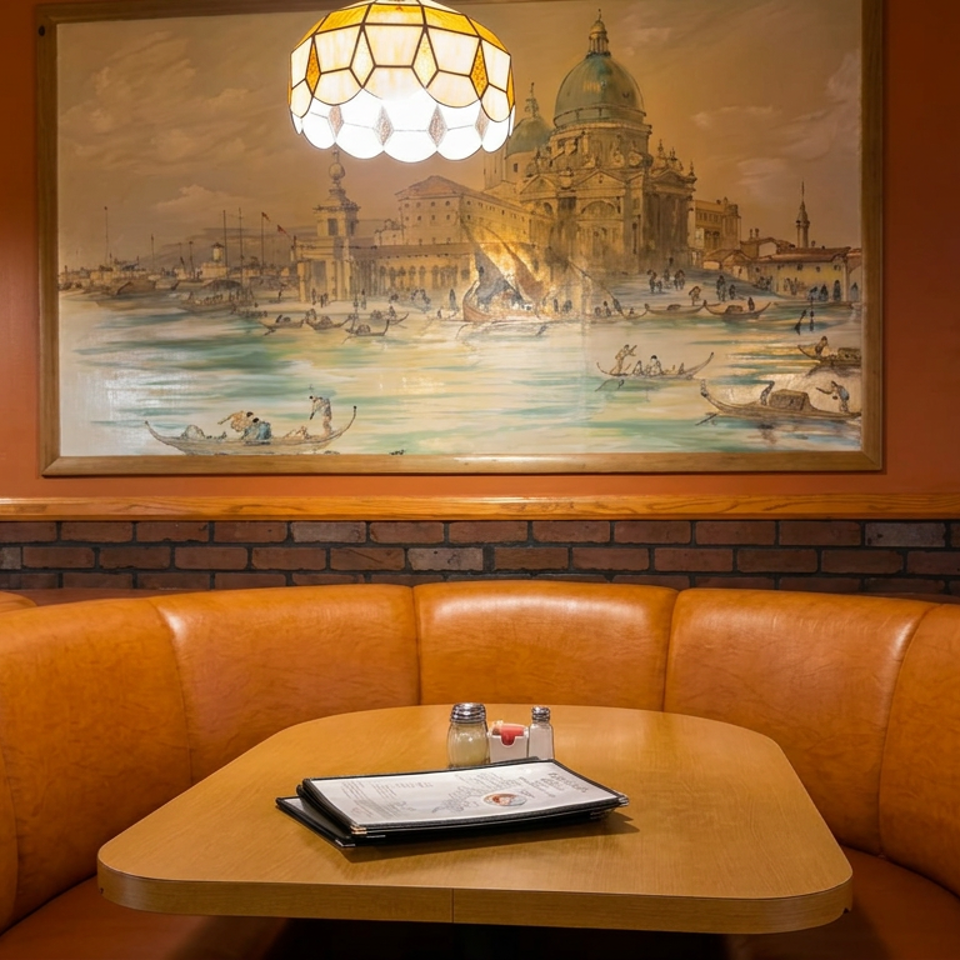 Warm restaurant dining booth with leather seating, menu, condiments, stained-glass lamp, and Mediterranean waterfront artwork.